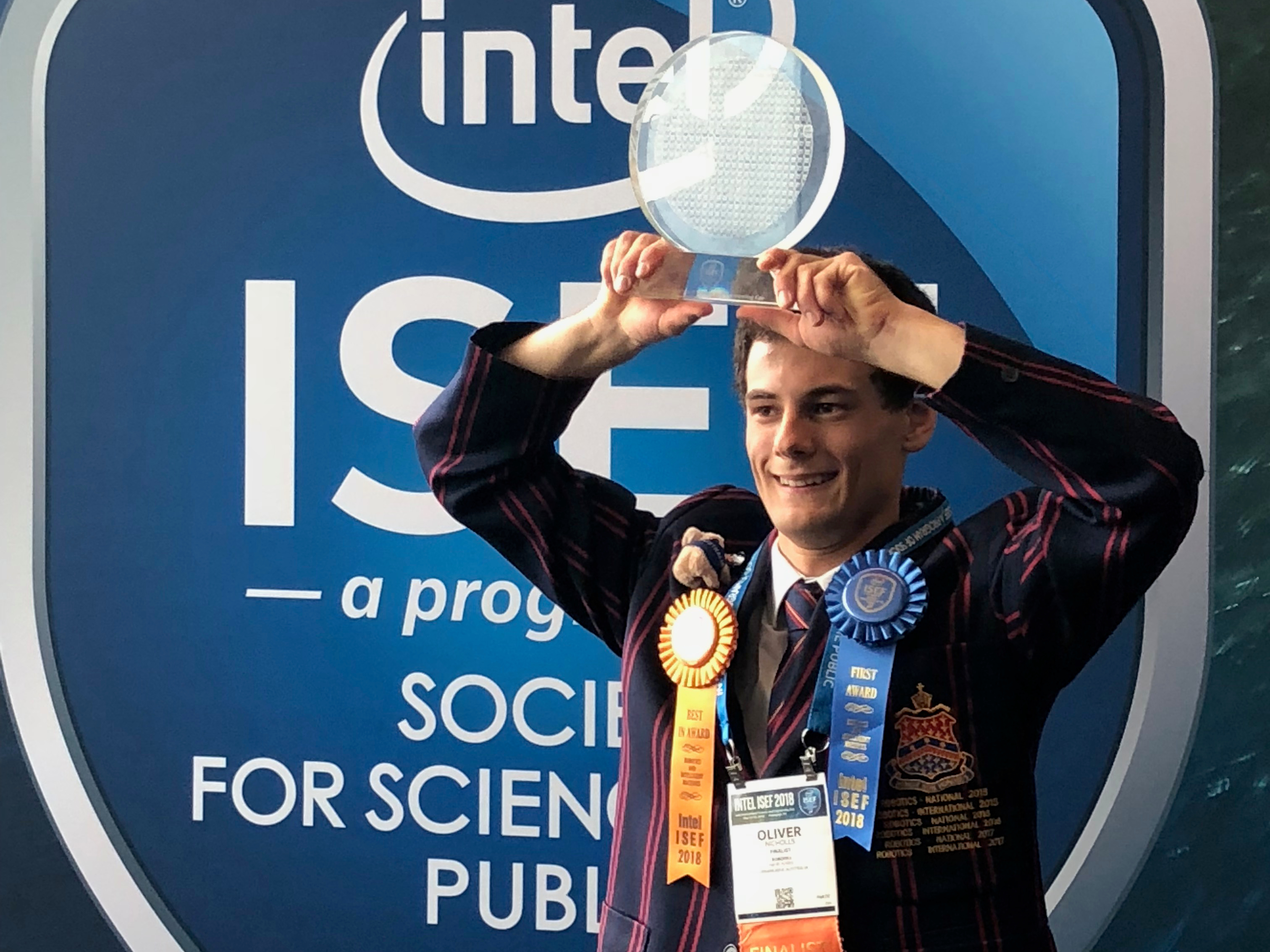 Oliver Nicholls holding trophy in front of Intel ISEF Banner.